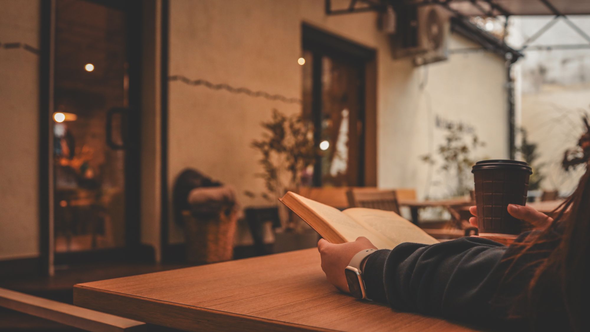 カフェのテーブルで本を読みながらコーヒーを飲んでいるところ